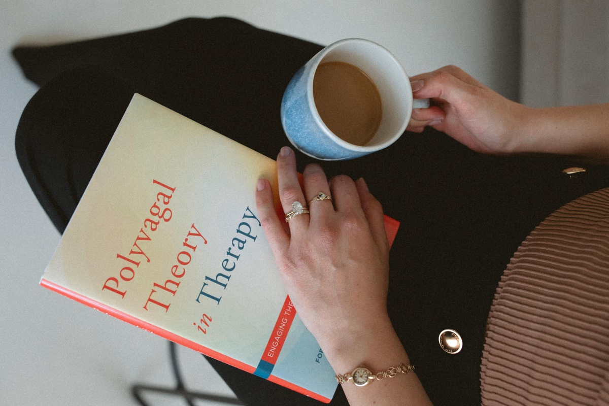 A copy of Polyvagal Theory in Therapy held with a ceramic mug, a trauma-informed reference text